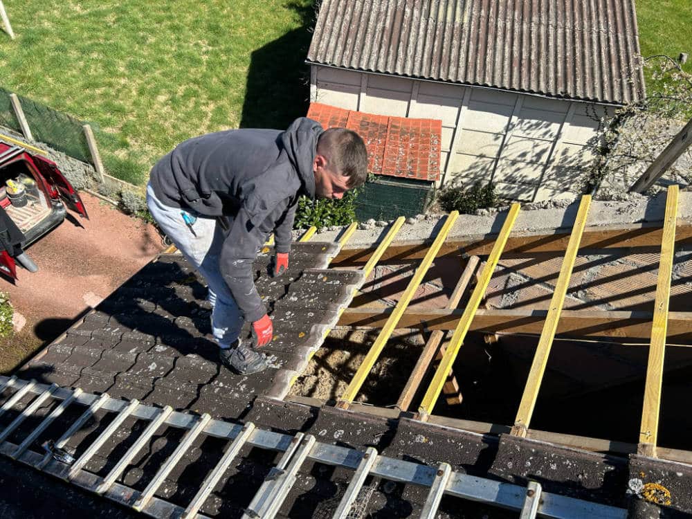 Vu sur un artisan en train de poser une toiture chantier de rénovation à Orléans, l'artisan est en train de retirer les tuiles anciennes pour les remplacer par de nouveaux matériaux